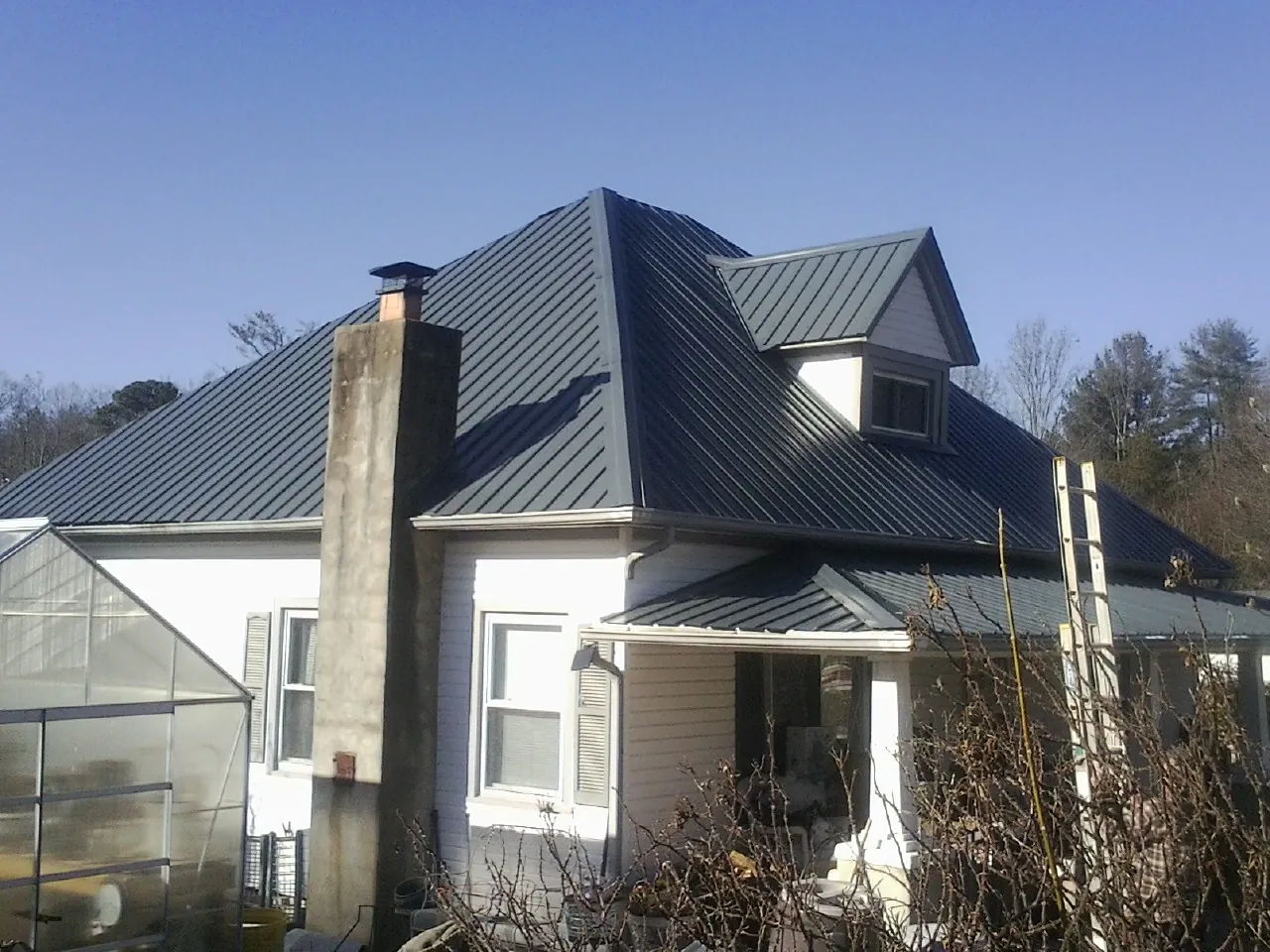 Dark blue standing seam metal roof on a white farmhouse with dormer — Slate & Tile Roof Repair by Roofing Brothers in Mc Louth