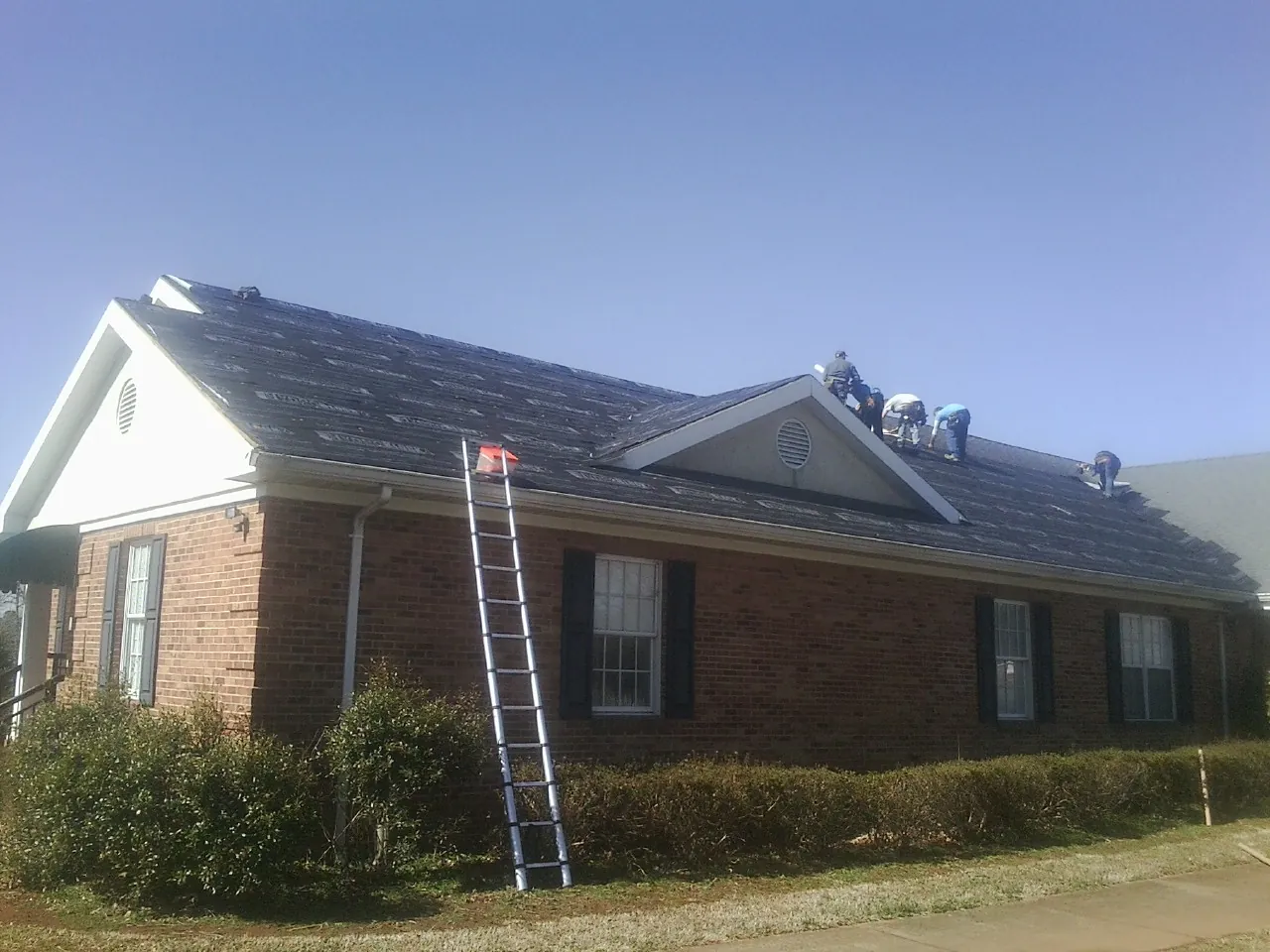 Crew tearing shingles off a brick ranch roof with a ladder set — Metal Roof Repair work by our crew in Mc Louth