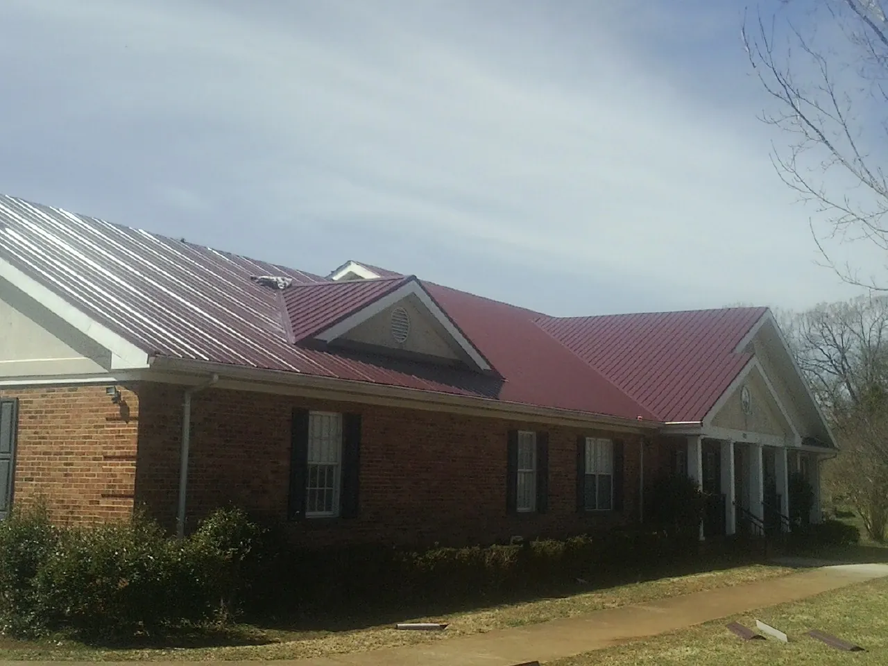 Red metal roof with gabled entries on a long brick building, from a Hail Damage Roof Repair job in Mc Louth