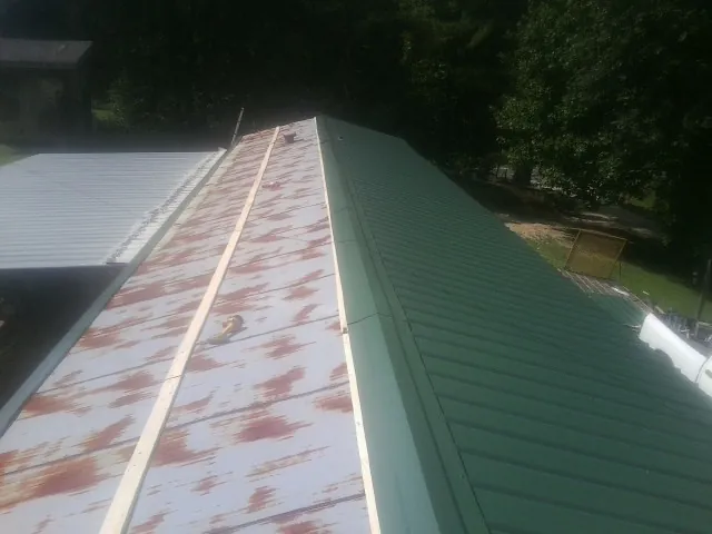 Old rusted panels beside newly installed green metal roofing — Wind Damage Roof Repair by Roofing Brothers in Mc Louth