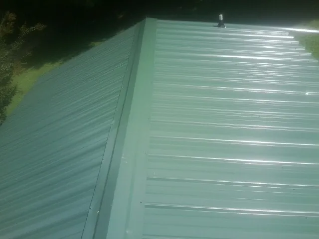 New green metal panels meeting at the ridge of a roof — Flat Roof Repair work by our crew in Mc Louth