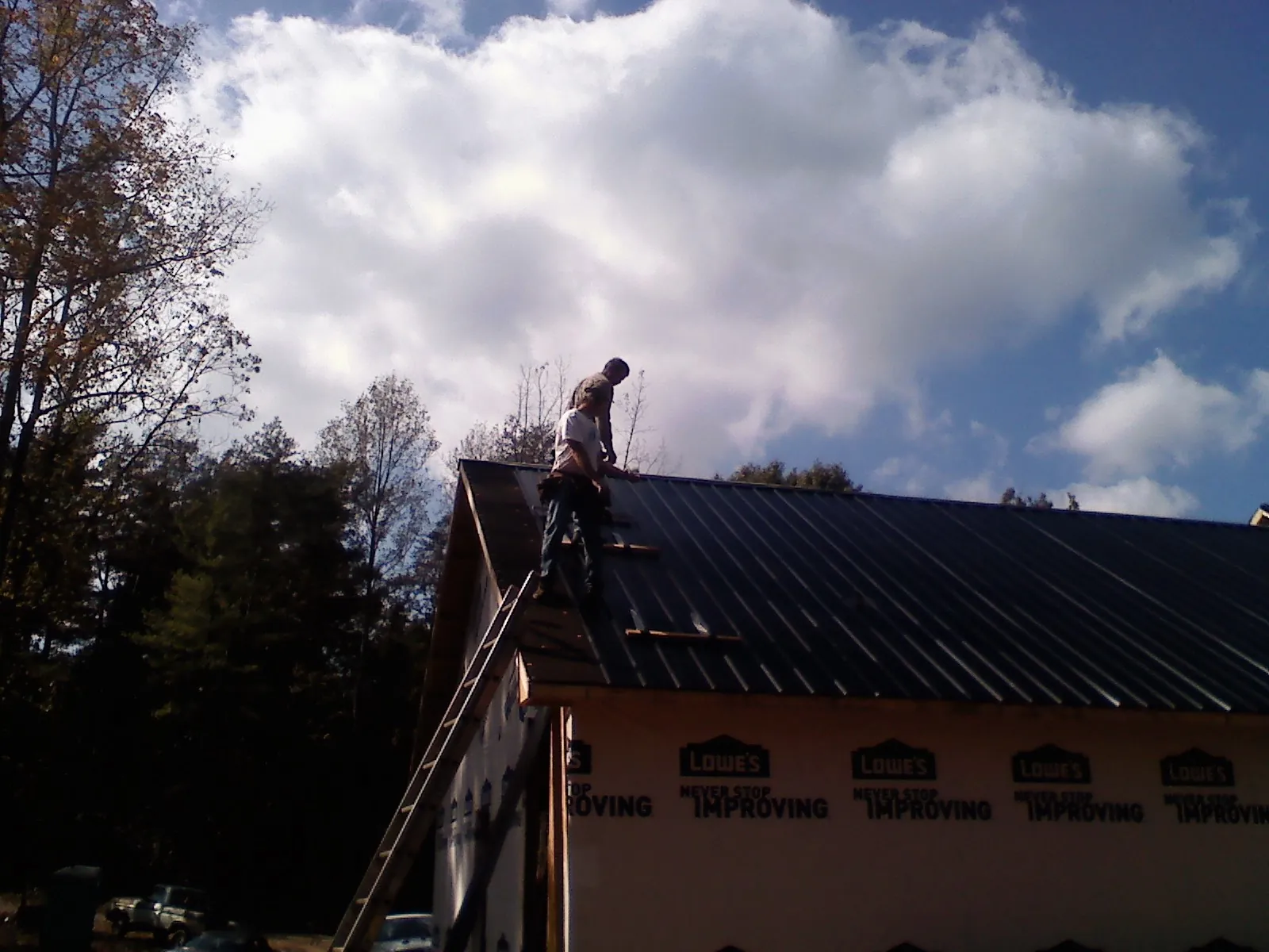 Roofer fastening dark metal panels high against a cloudy sky, from a Roof Inspection job in Mc Louth