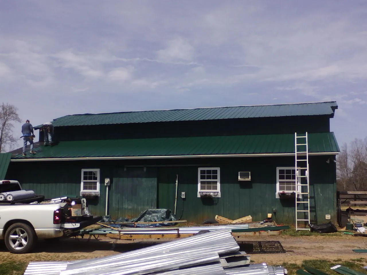 Crew installing green metal roofing on a large green barn in Mc Louth