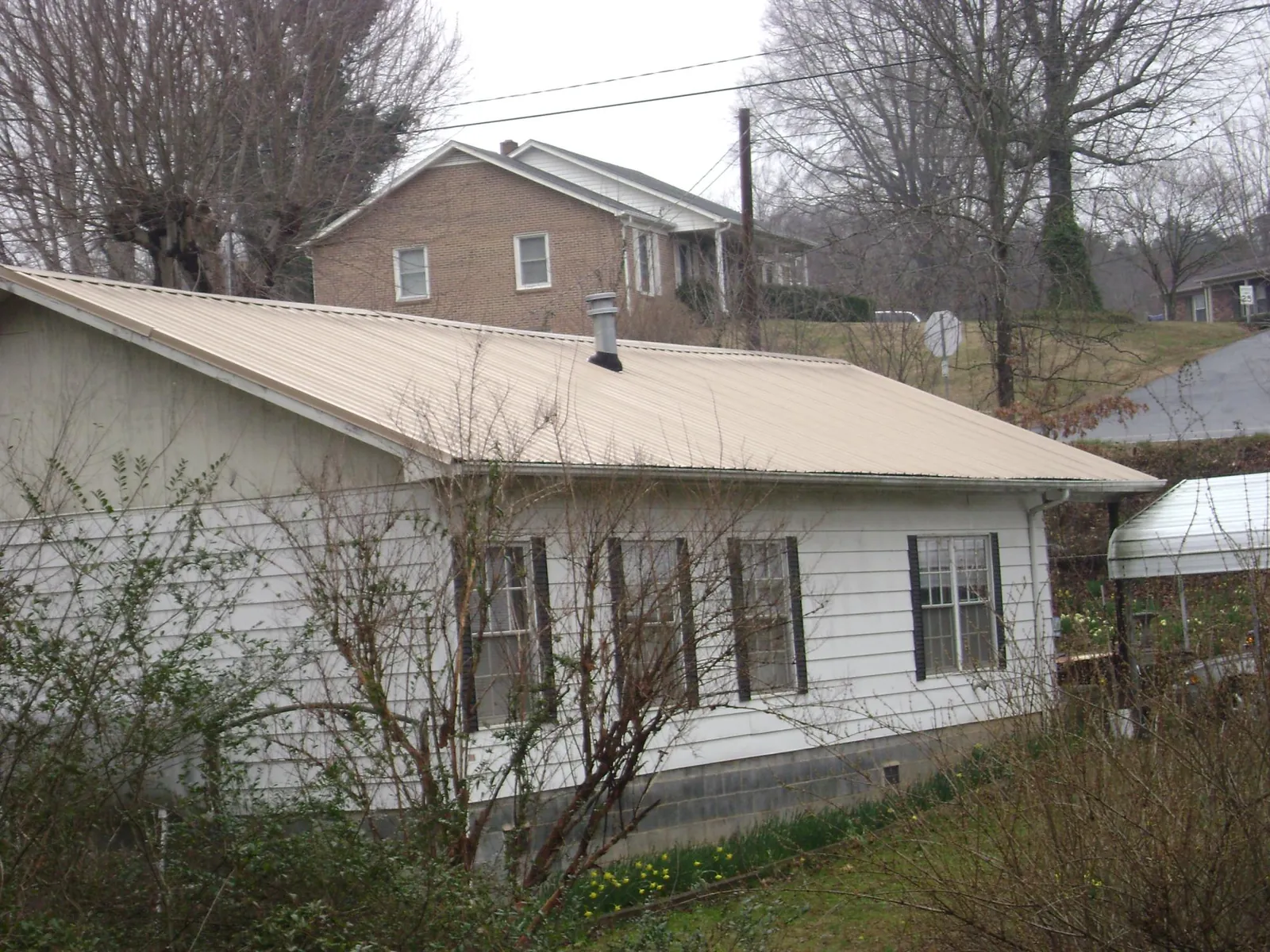 Tan metal roof on a white sided house set into a hillside — Commercial Roofing by Roofing Brothers in Mc Louth