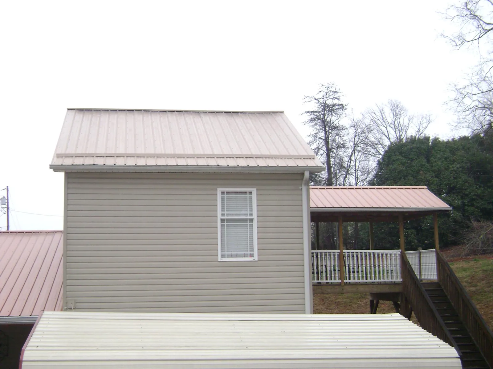 Tan metal roofs on a two story addition and attached porch, from a Roof Replacement job in Mc Louth